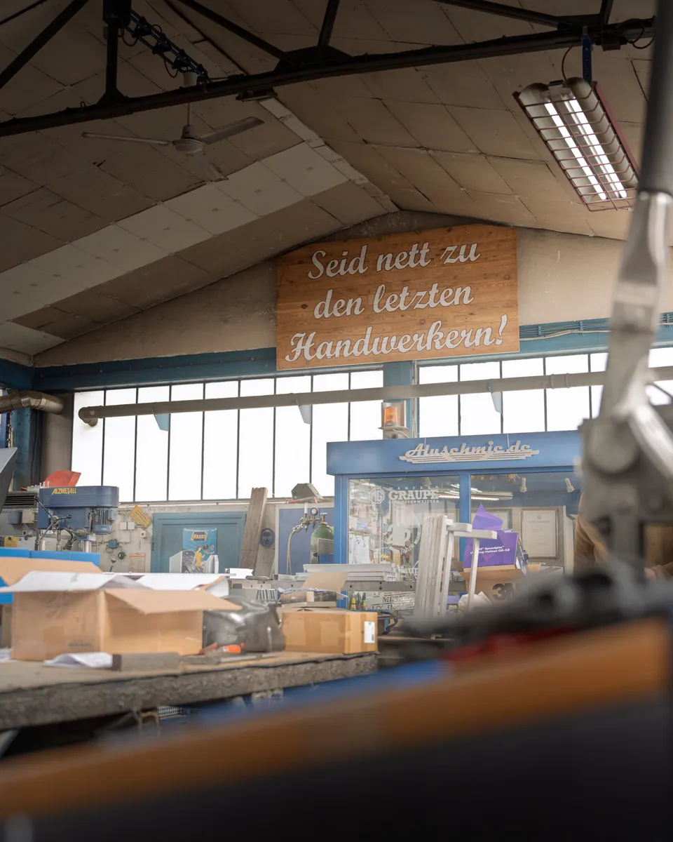 Holzschild „Seid nett zu den letzten Handwerkern!“ unter dem Hallendach