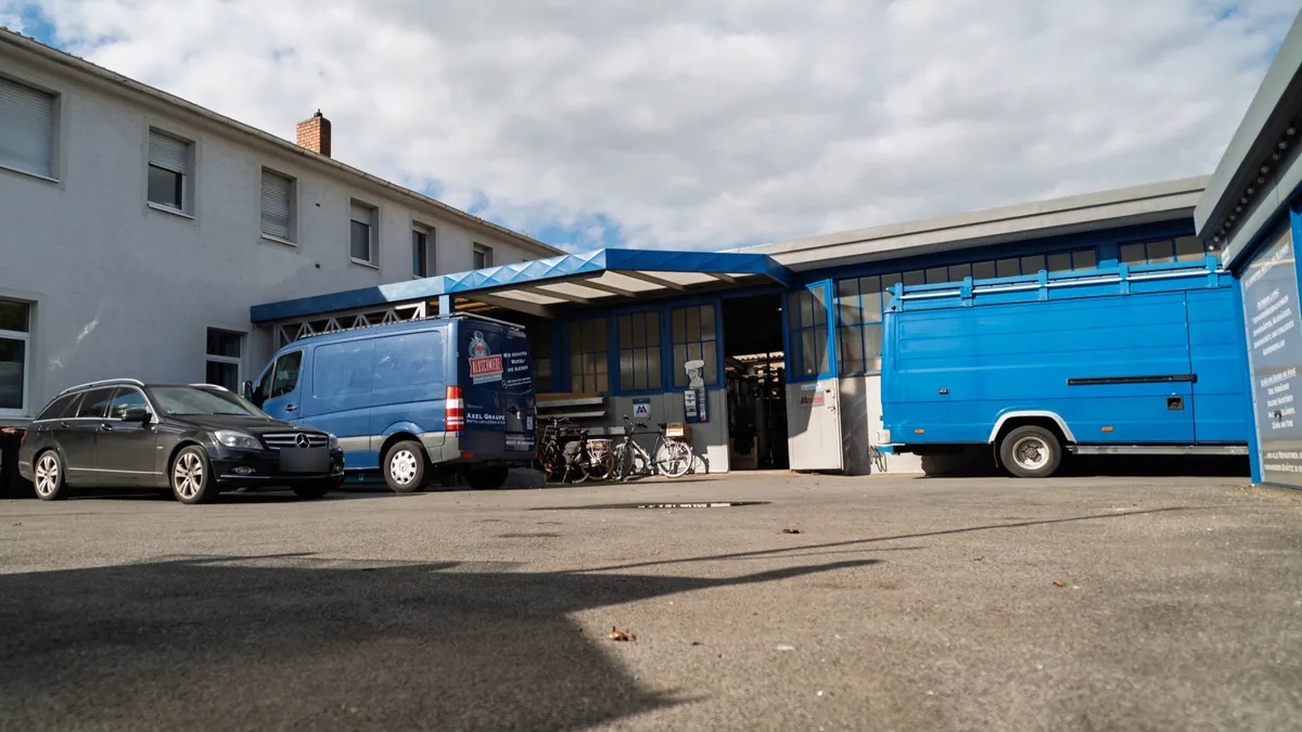 Hof der Aluschmiede mit Werkstattgebäude, blauem Vordach und Firmenwagen
