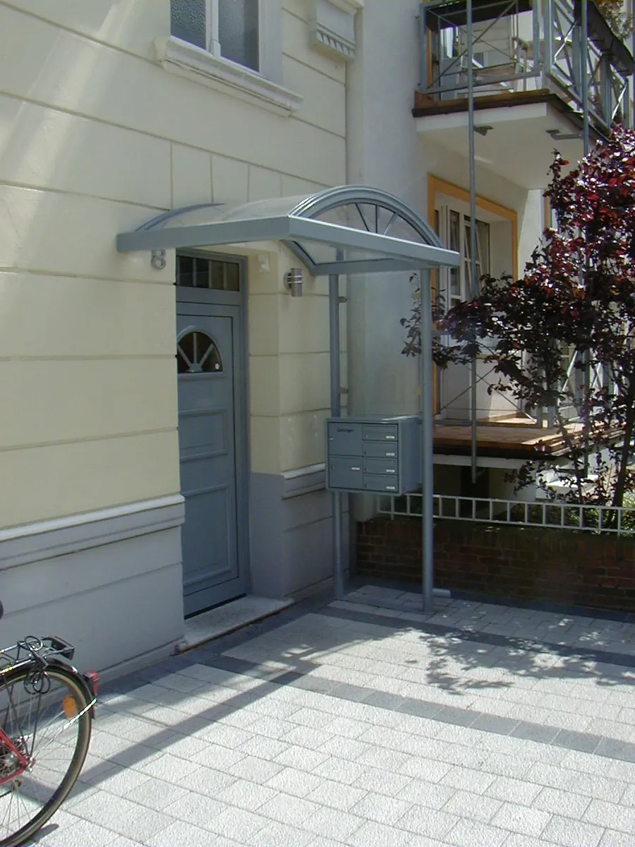 Glasvordach mit Rundbogen an einem Mehrfamilienhaus